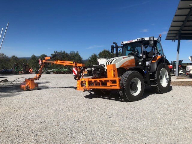 Traktor mit Anbaugerät auf Kiesplatz, ideal für Landwirtschaft und Gelände, bei strahlendem Sonnenschein.