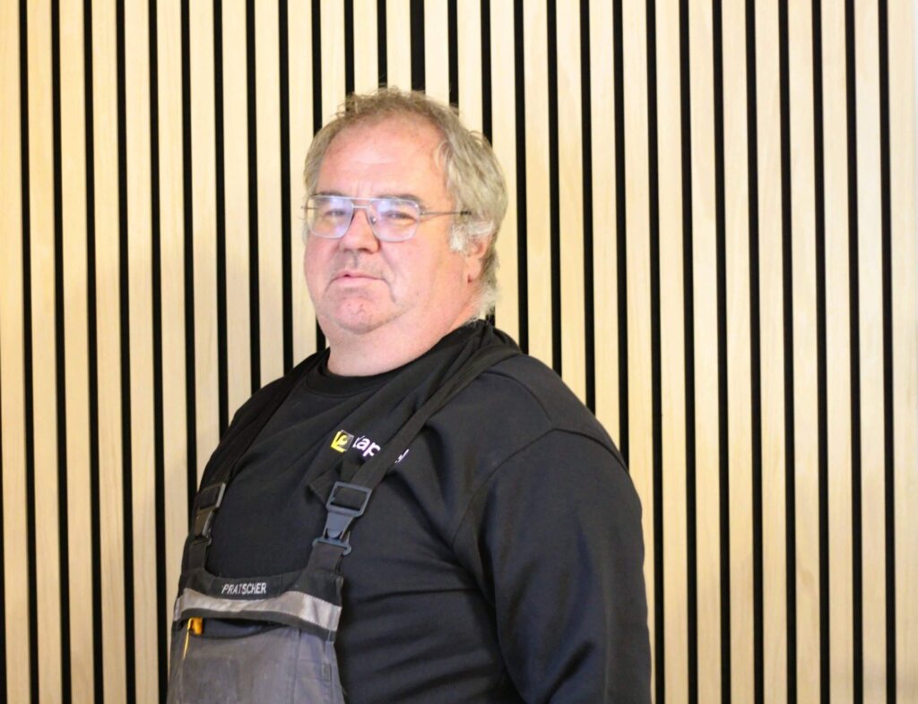 Handwerker im Arbeitsanzug steht vor moderner, vertikaler Holzverkleidung.