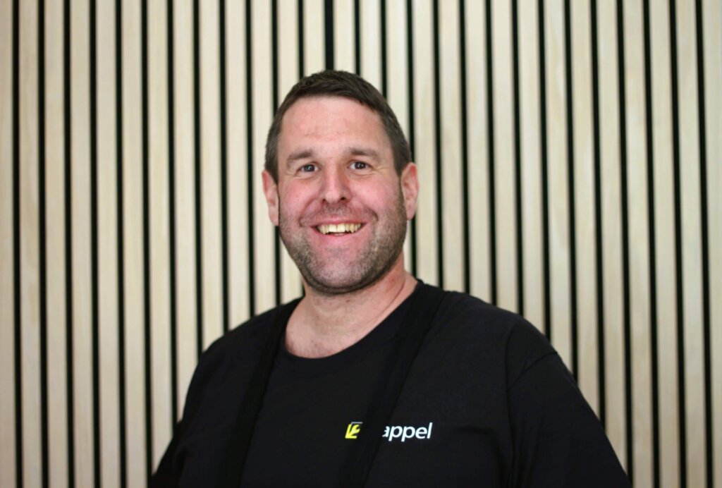Freundlich lächelnder Mann vor Holzlamellen-Hintergrund im schwarzen T-Shirt von Eppel.