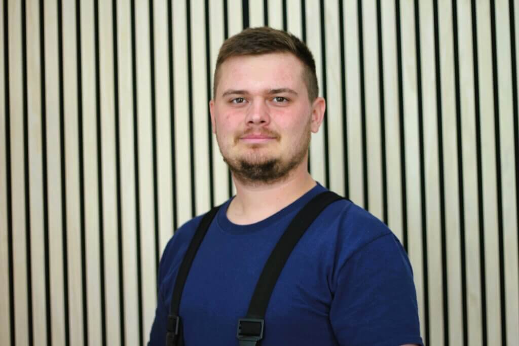 Person in blauem T-Shirt vor gestreiftem Hintergrund betrachtet direkt die Kamera.