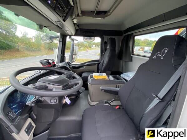 Fahrerkabine eines Lastwagens mit ergonomischem Interieur und modernem Armaturenbrett, Außenblick auf die Straße.