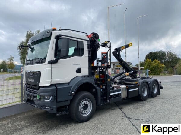 Weißer MAN-LKW mit Ladekran auf Industrieplatz, bewölkter Himmel im Hintergrund. Ideal für Schwertransporte.