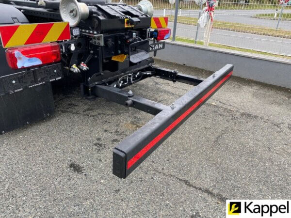 LKW-Unterfahrschutz an einem MAN-Fahrzeug, seitliche Ansicht auf Asphalt, mit rotem Reflektorstreifen.