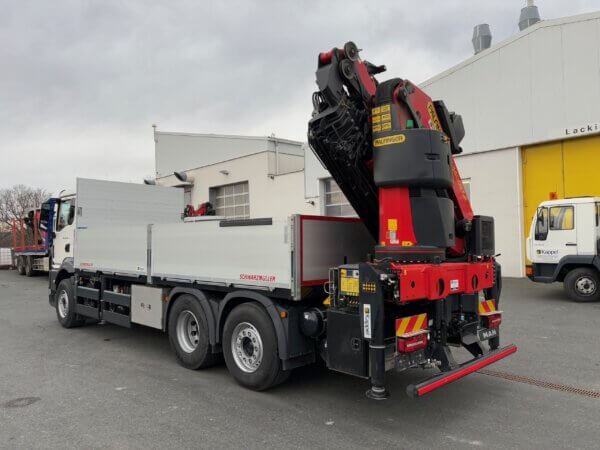 LKW mit montiertem Kran auf einem Industriehof, bereit für den Transport schwerer Lasten.