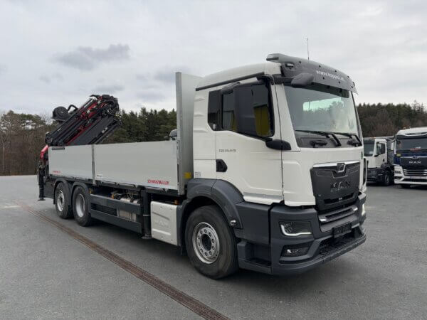 Moderner MAN-LKW mit Ladekran von Schwarzmüller auf einem Parkplatz, umgeben von Wald. Ideal für Baustellenarbeit.