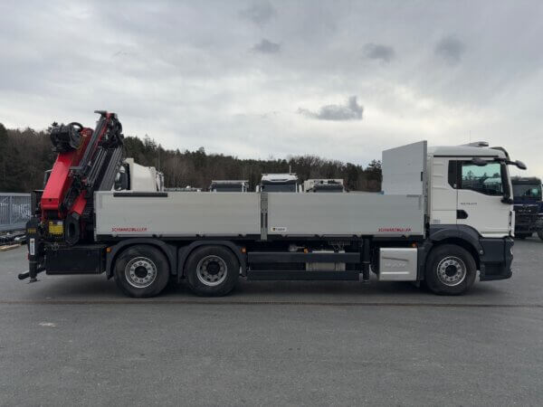 LKW mit Kranaufbau von Schwarzmüller, seitlich abgebildet auf einem Parkplatz, bewölkter Himmel im Hintergrund.
