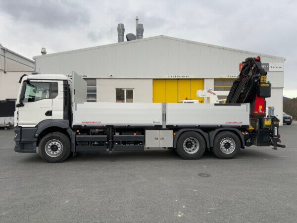 Lkw mit Kranaufbau von Schwarzmüller vor einem Werkstattgebäude, ideal für Baueinsätze.