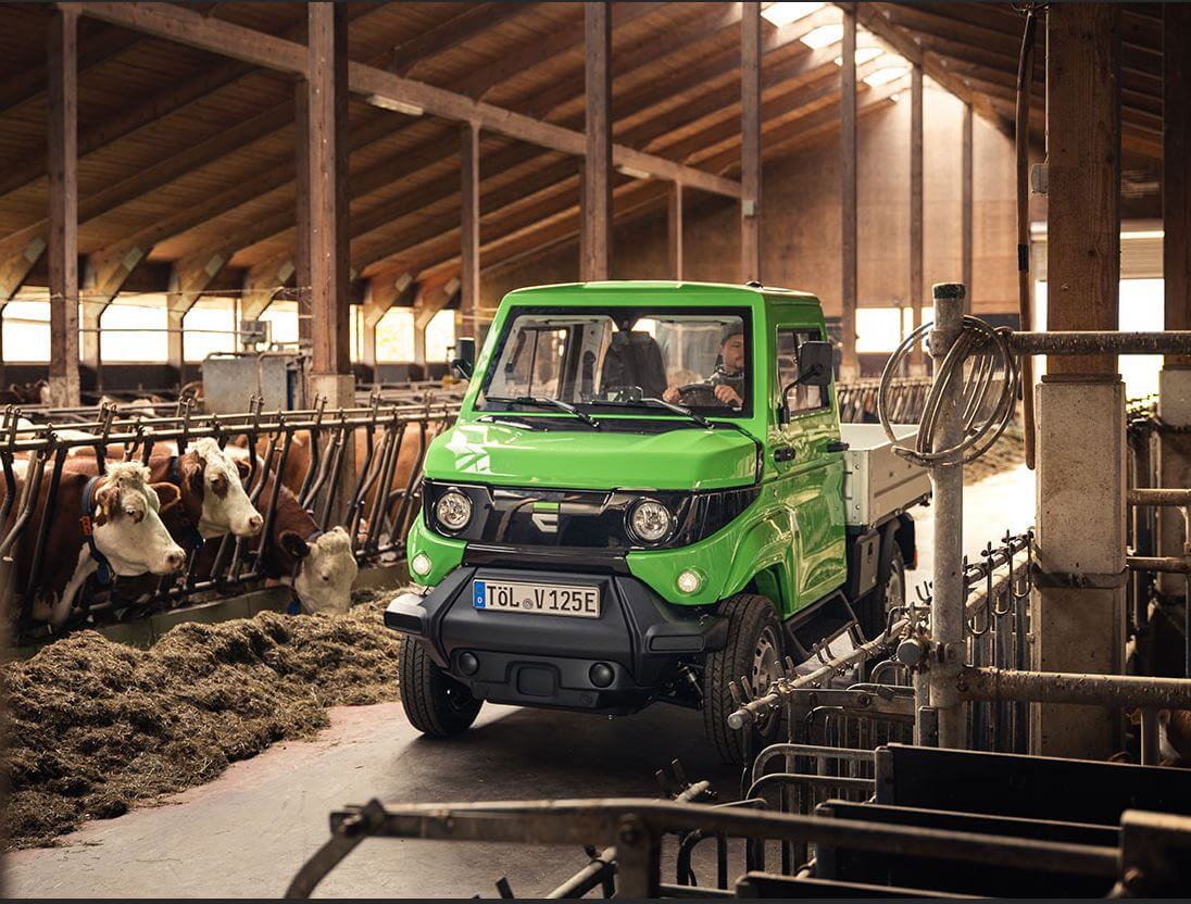 Grünes Elektrofahrzeug im Kuhstall, umgeben von Vieh, in einer ländlichen Scheune. Ideal für nachhaltige Landwirtschaft.