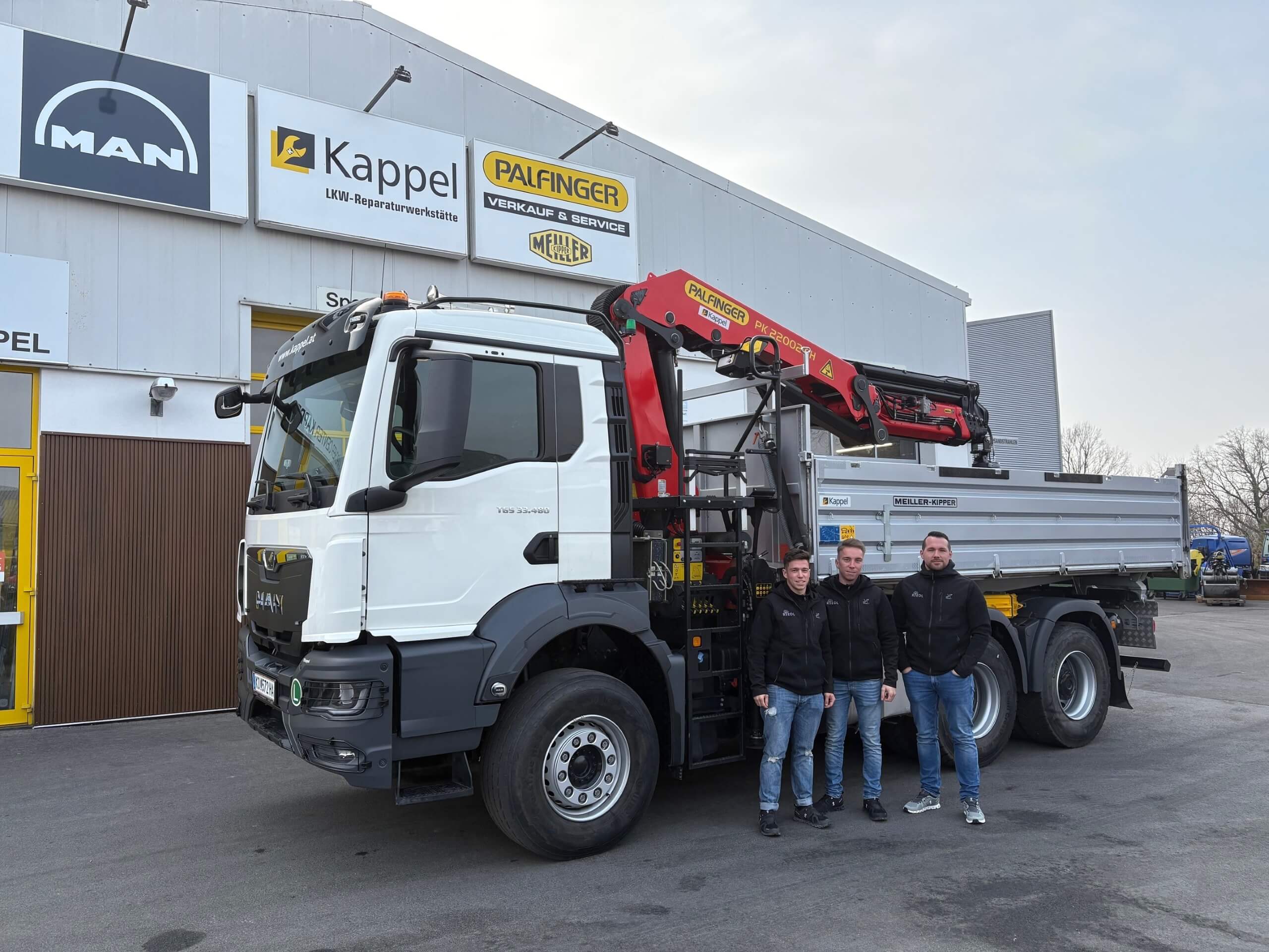 LKW mit Kran bei Kappel-Reparaturwerkstätte; drei Männer davor posieren in Arbeitskleidung.