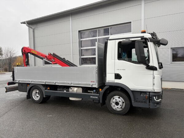 LKW mit rotem Kran auf Parkplatz vor grauer Halle, ideal für Baustellen- und Transportarbeiten.