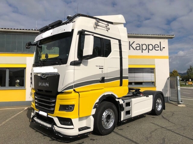 Moderner MAN-Truck in Gelb-Weiße Lackierung vor Kappel-Gebäude bei sonnigem Wetter. Ideal für Transportlogistik.