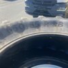 Großer Fahrzeugreifen mit der Aufschrift 650/65 R 38, im Hintergrund steht ein Fahrzeug auf Asphalt.