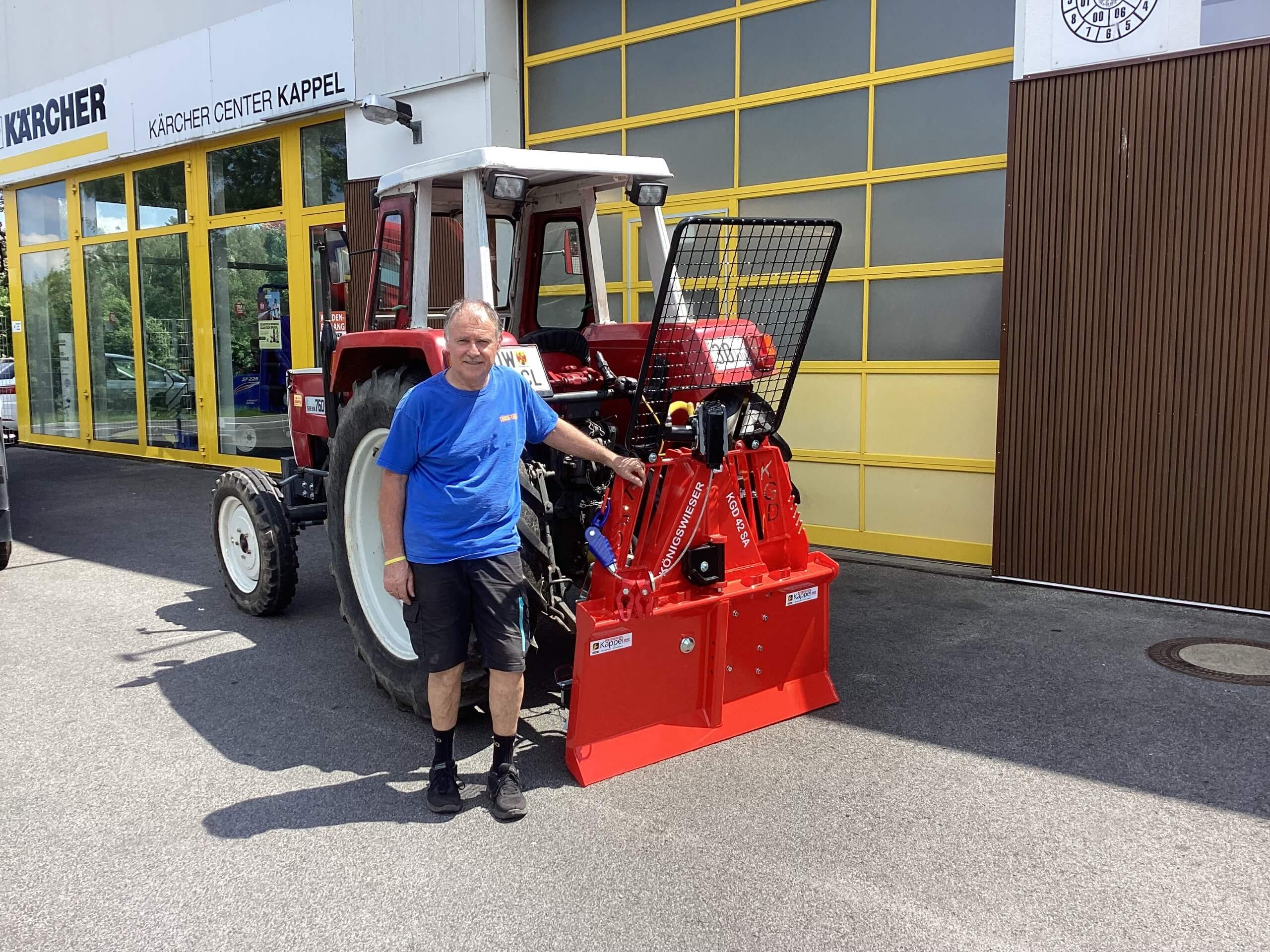 Person neben Traktor mit roter Anbauvorrichtung vor einem Kärcher Center Gebäude.