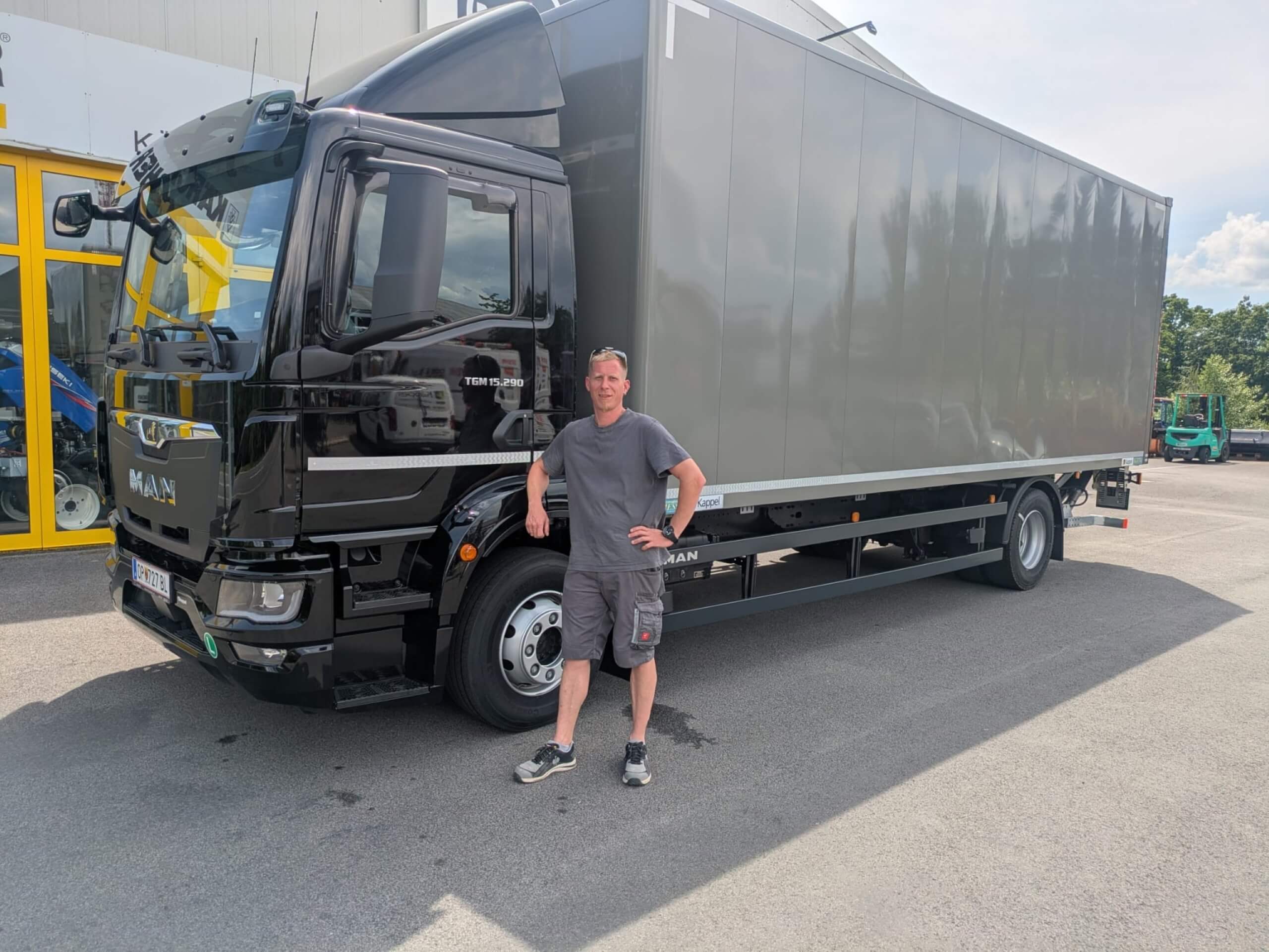 Mann steht vor schwarzem MAN-Lkw, sonniger Tag, Parkplatz, moderne Nutzfahrzeugtechnologie, Transportlösung.