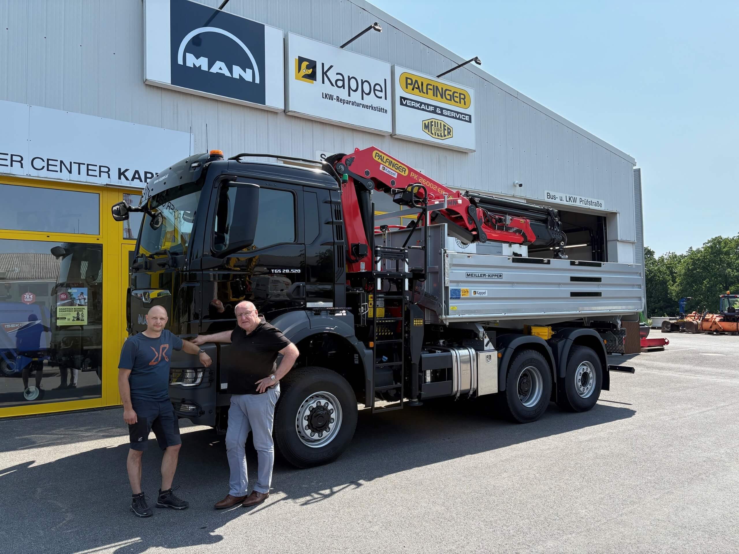 Zwei Männer vor einem MAN-LKW mit Palfinger-Kran bei Kappel Nutzfahrzeuge, sonniger Tag, Gebäude im Hintergrund.