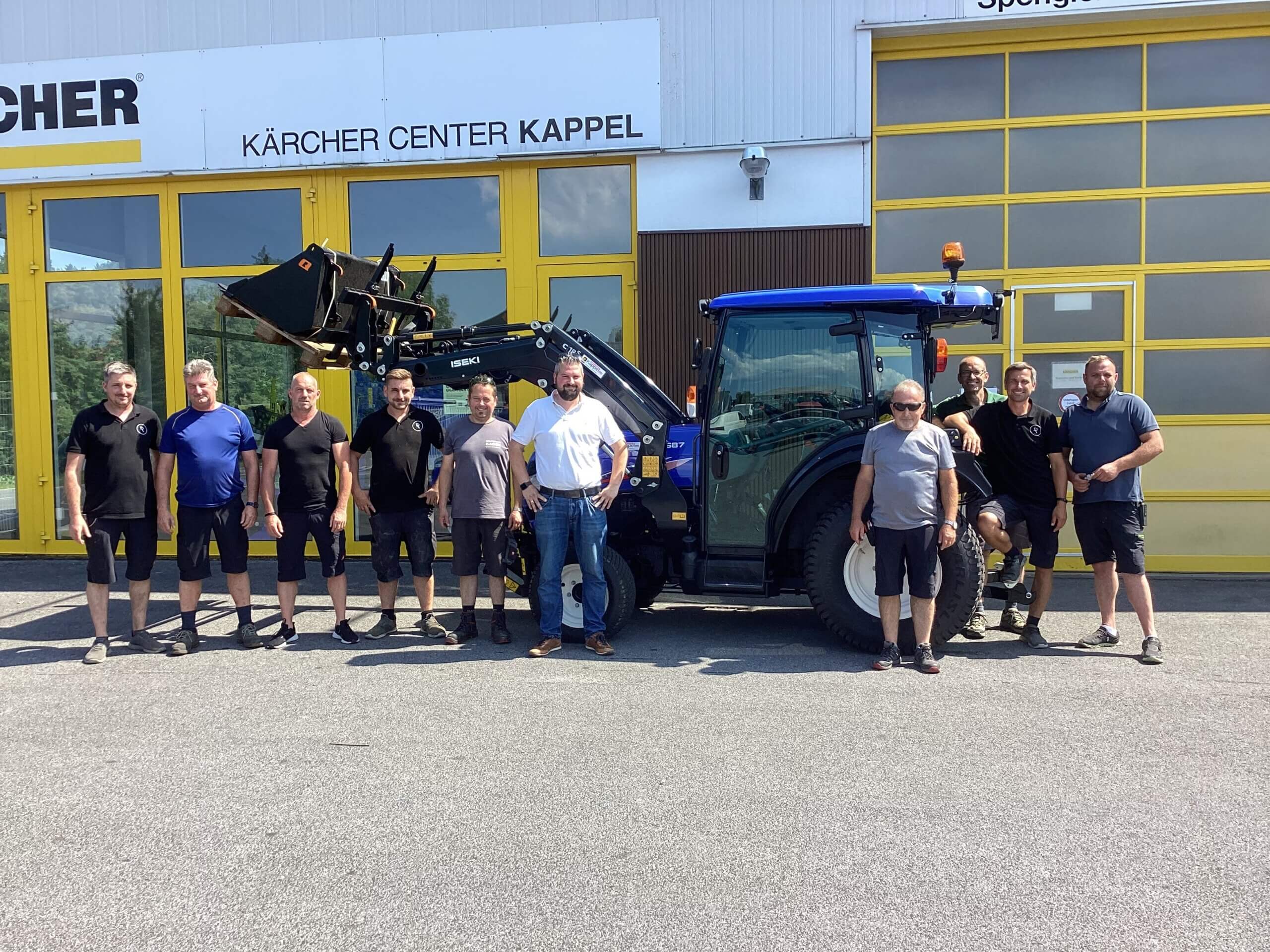 Mitarbeiterteam posiert vor einem blauen Traktor beim Kärcher Center Kappel an einem sonnigen Tag.
