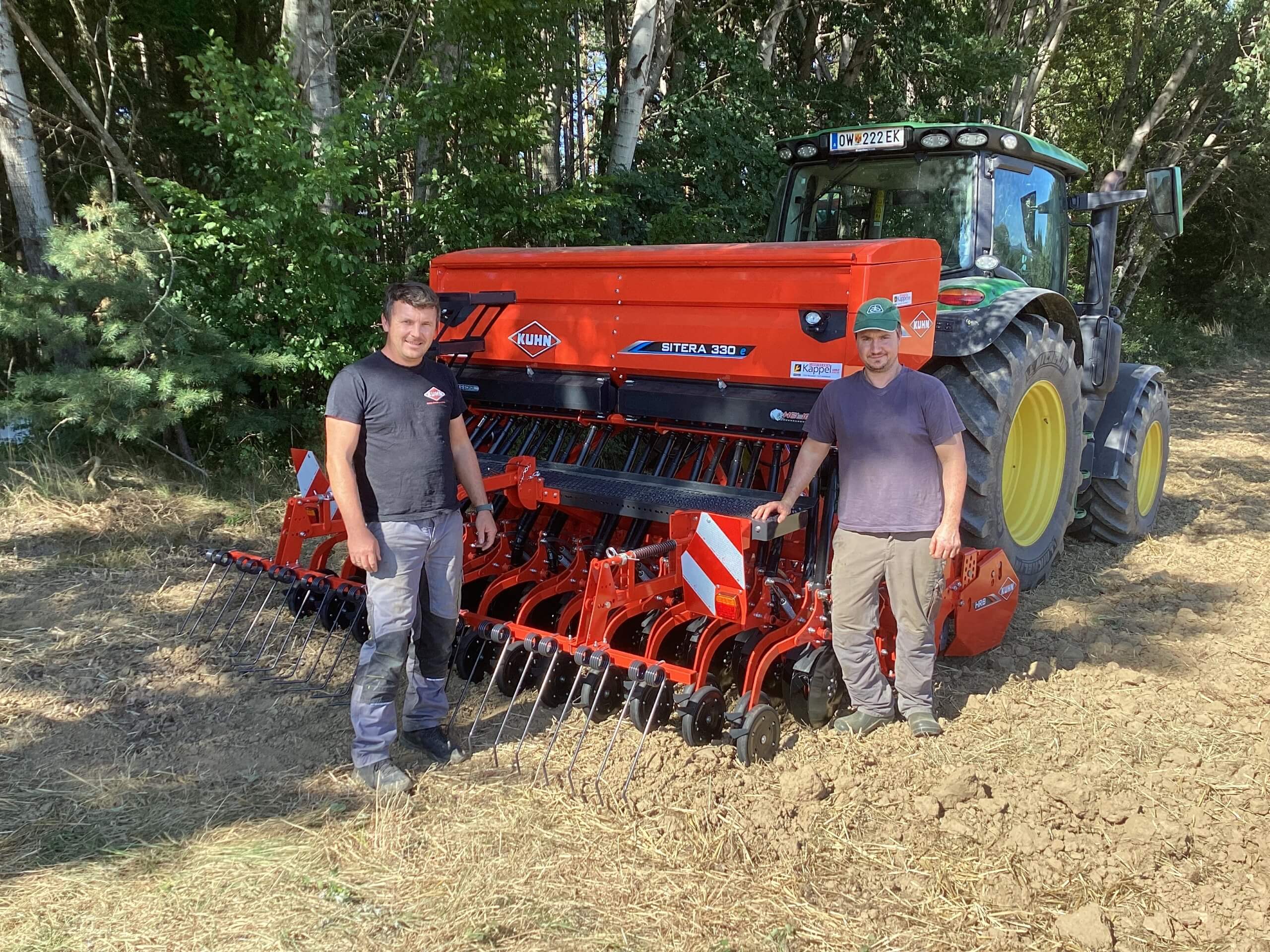 Zwei Landwirte vor einer KUHN Sitera 330S Maschine und einem Traktor auf einem Feld.