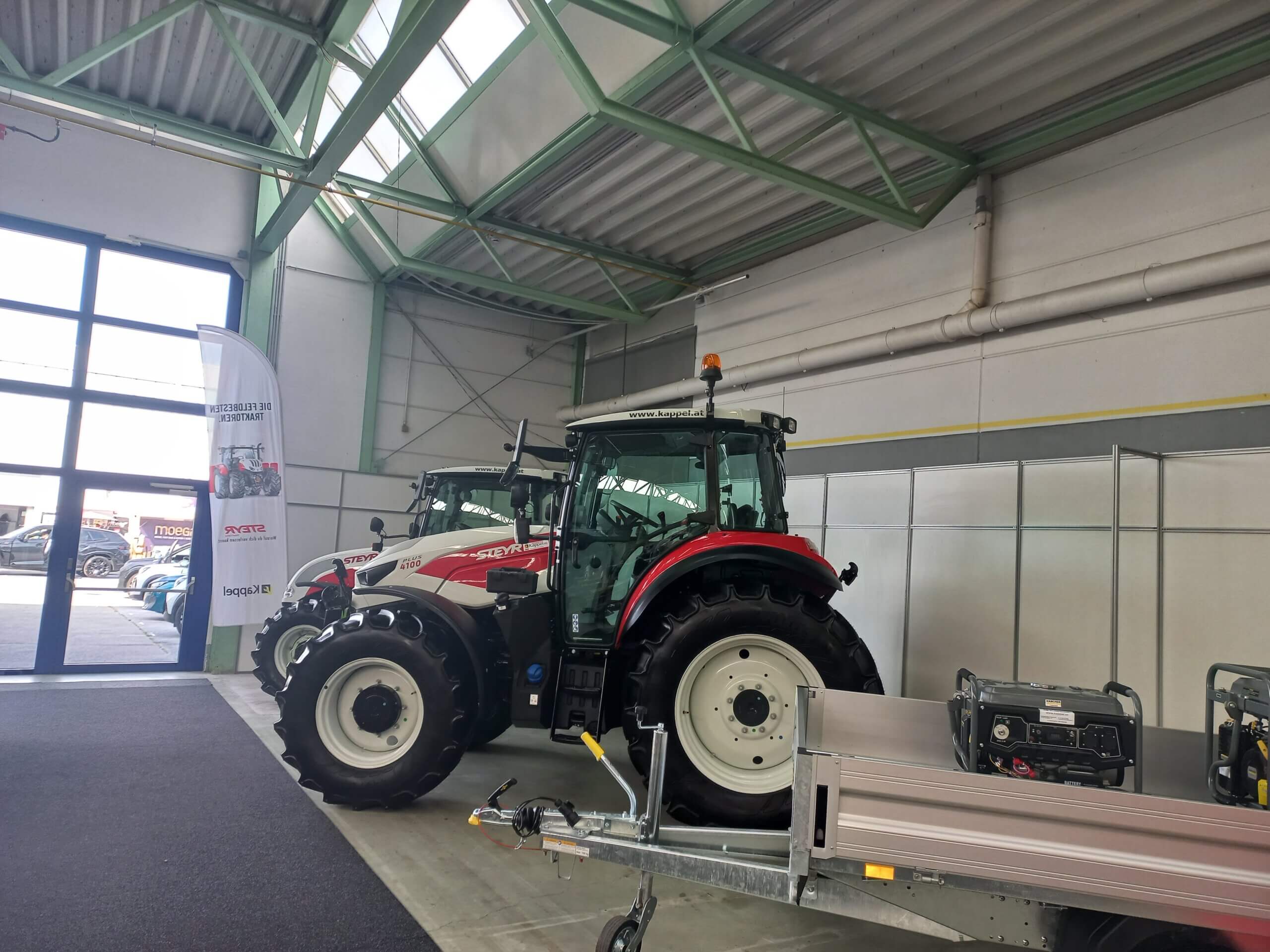 Moderner roter Traktor in einer Ausstellungshalle mit Traktorzubehör und Informationsbanner.
