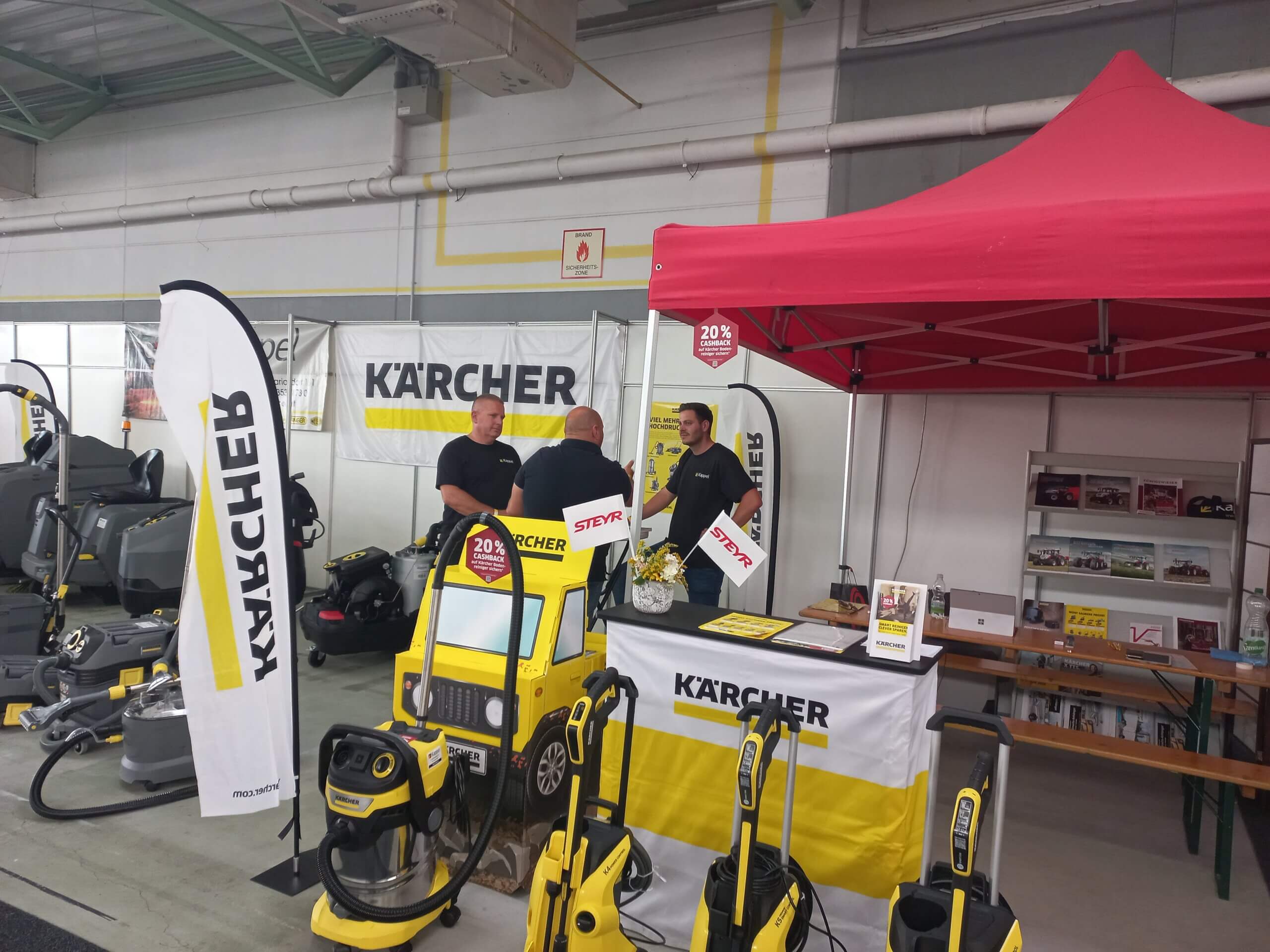 Kärcher-Stand auf Messe mit Reinigungsgeräten und Personal unter rotem Pavillon, Produkte im Vordergrund.