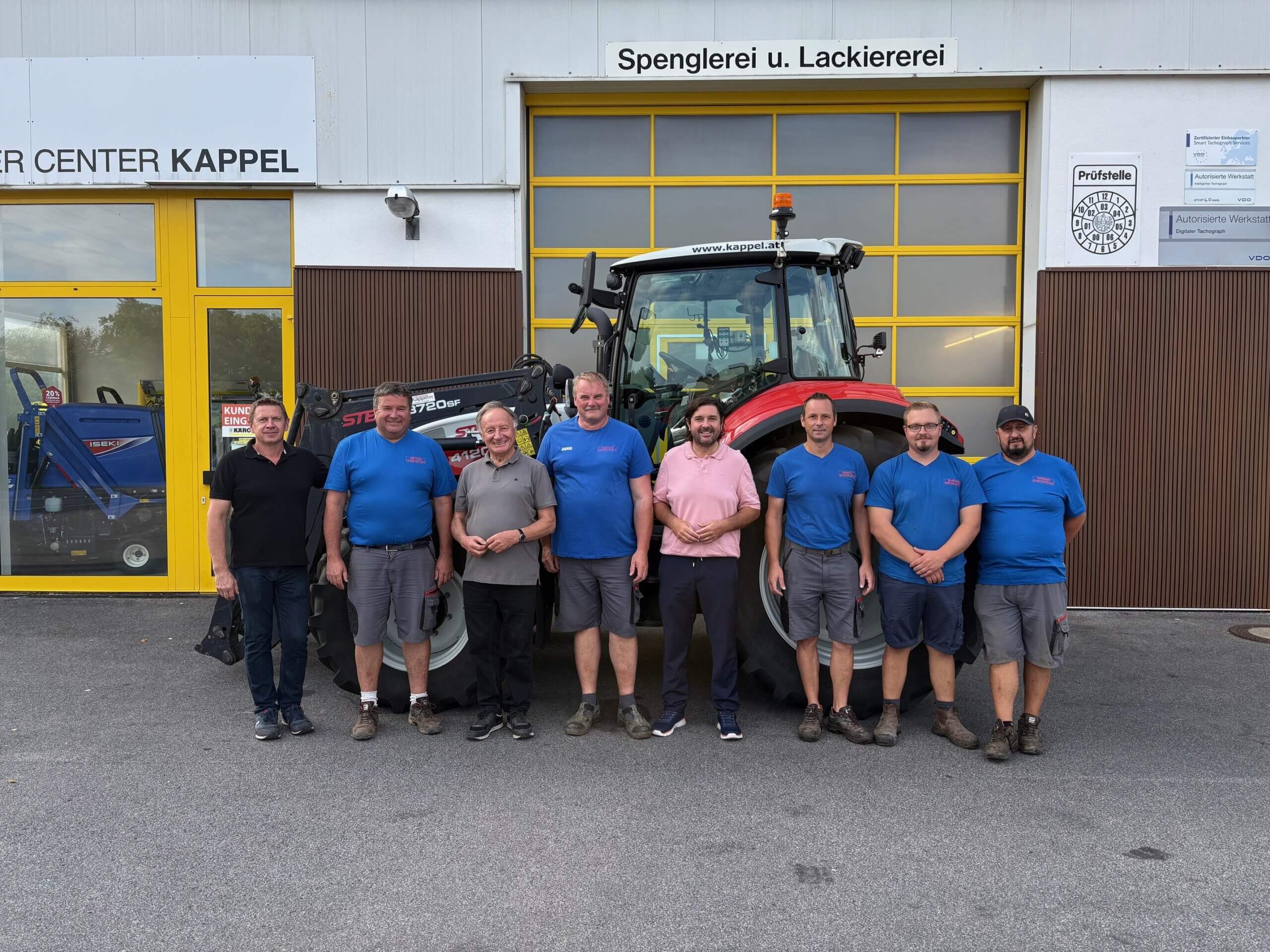 Eine Gruppe von Männern vor einem Traktor bei einer Spenglerei und Lackiererei in Kappel.