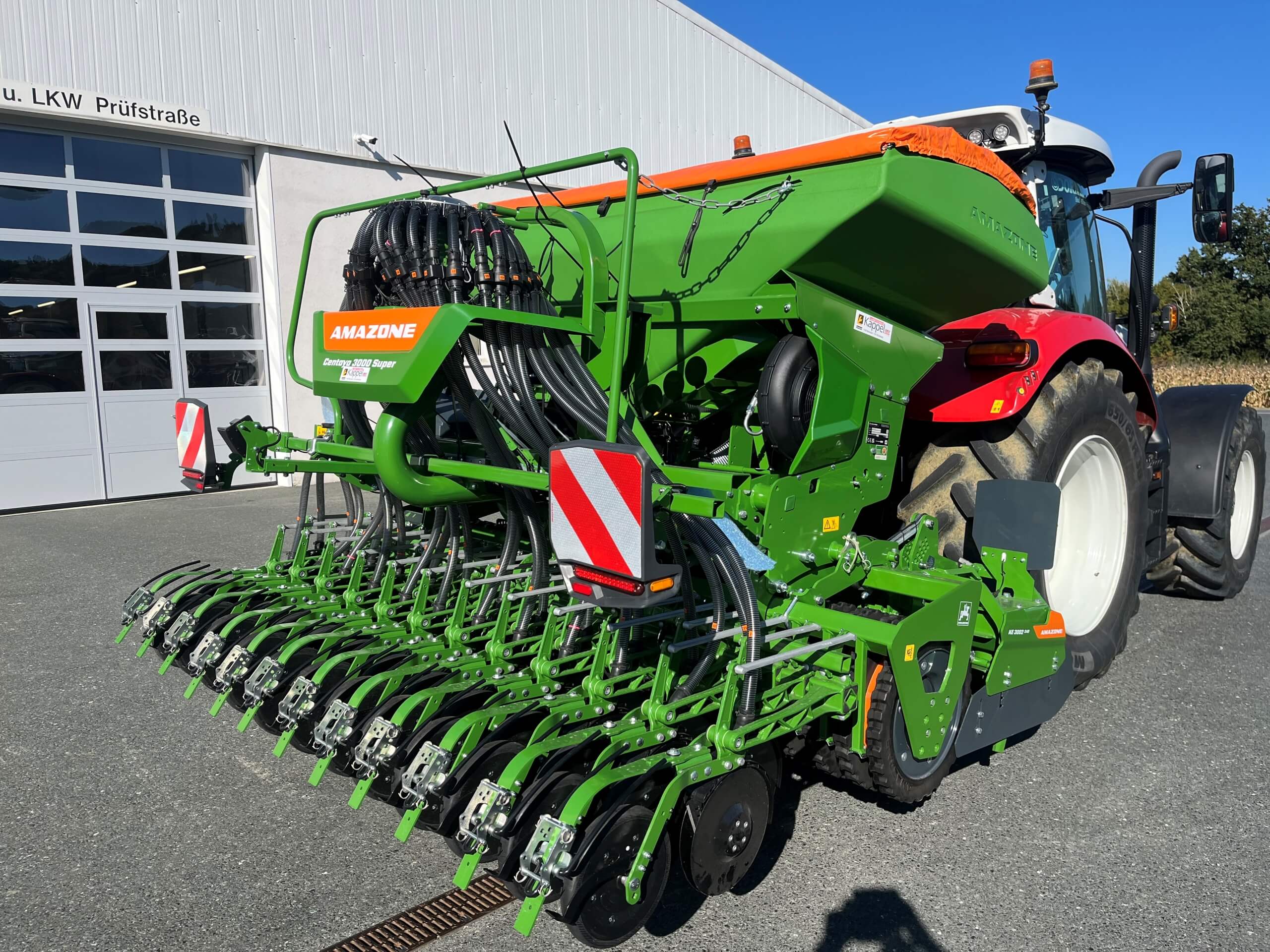 Grüne Amazone Sämaschine angehängt an einen Traktor vor einem modernen Gebäude bei Sonnenschein.