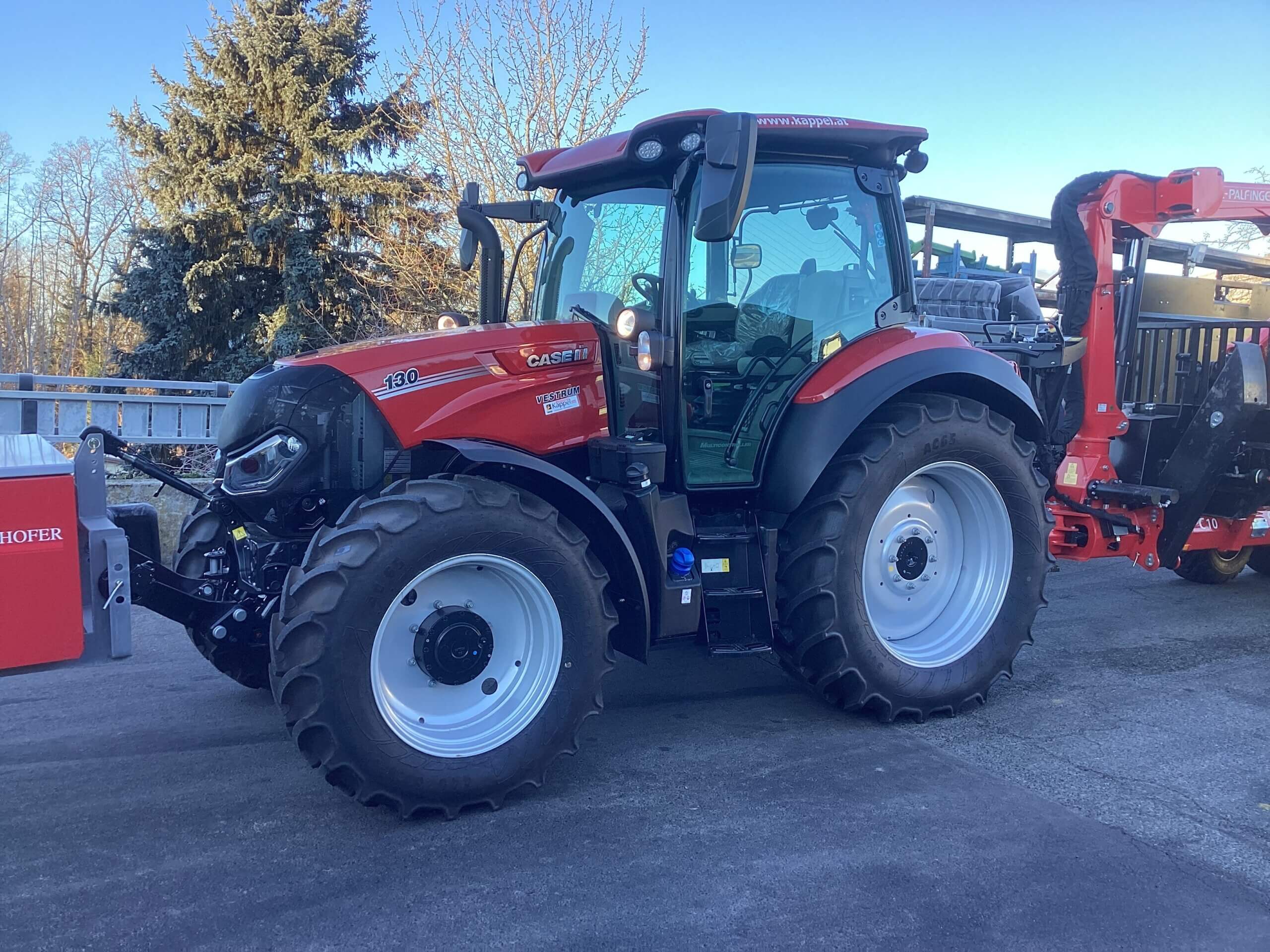 Roter Traktor mit großen Reifen und landwirtschaftlichem Anbaugerät auf einer Straße bei Tageslicht.